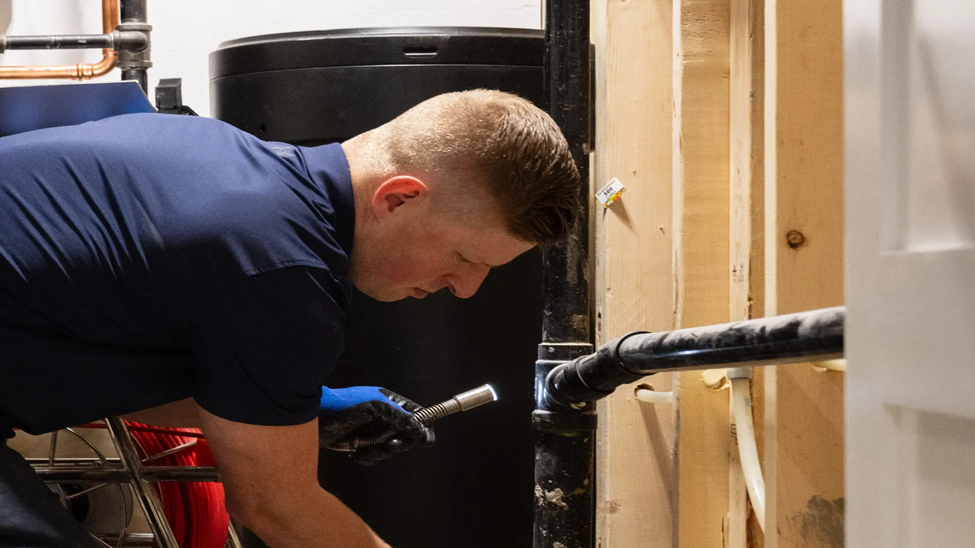 Technician-Inspecting-Black-Drain-Pipe-With-Flashlight