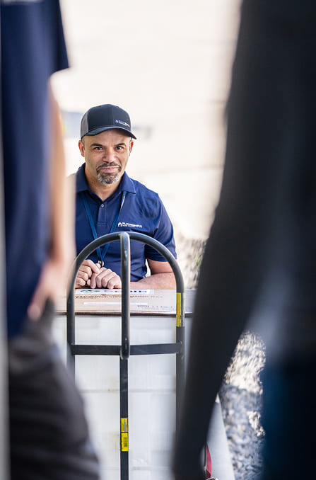 Technician-Delivering-Equipment-On-Hand-Truck-To-Home